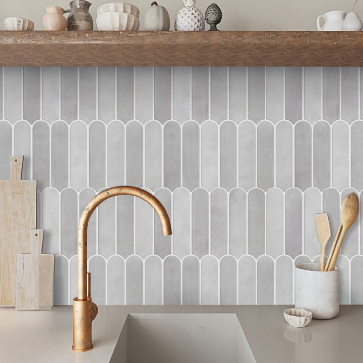 Gray scalloped tile backsplash behind a matte copper kitchen faucet and sink, with a wooden shelf and kitchen decor above.