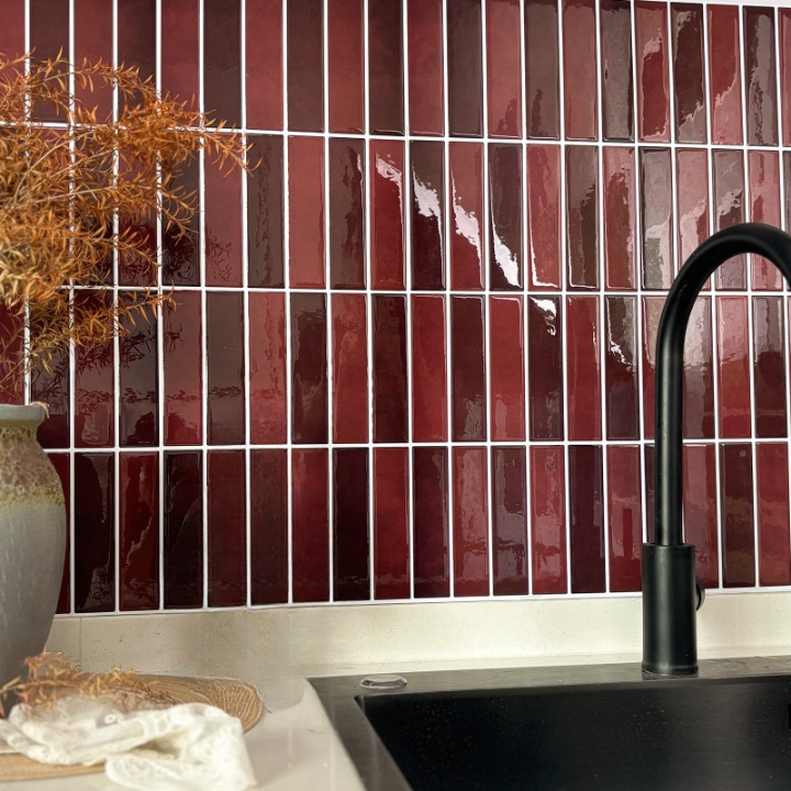 Glossy rectangular subway tiles in a deep burgundy red color arranged on a kitchen backsplash, with a black faucet and sink in the foreground.