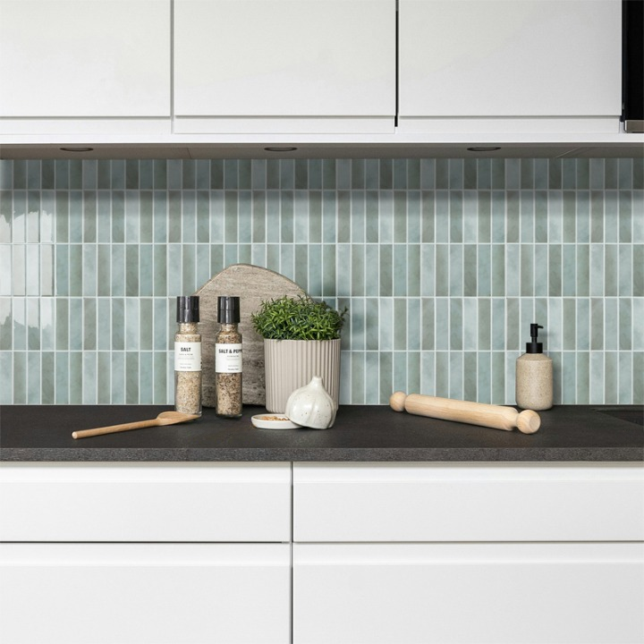 Modern kitchen with white cabinets, black countertop, and green tiled backsplash.